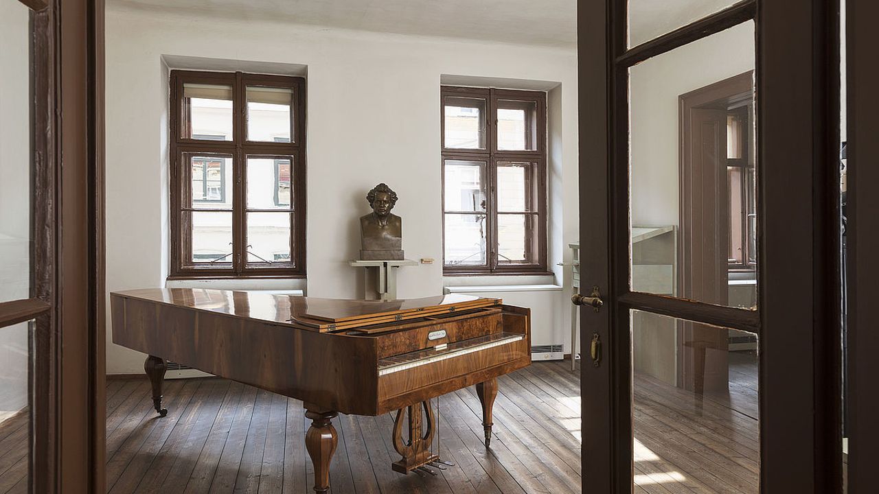 Innenraum von Schuberts Sterbewohnung mit einem braunen Flügelklavier