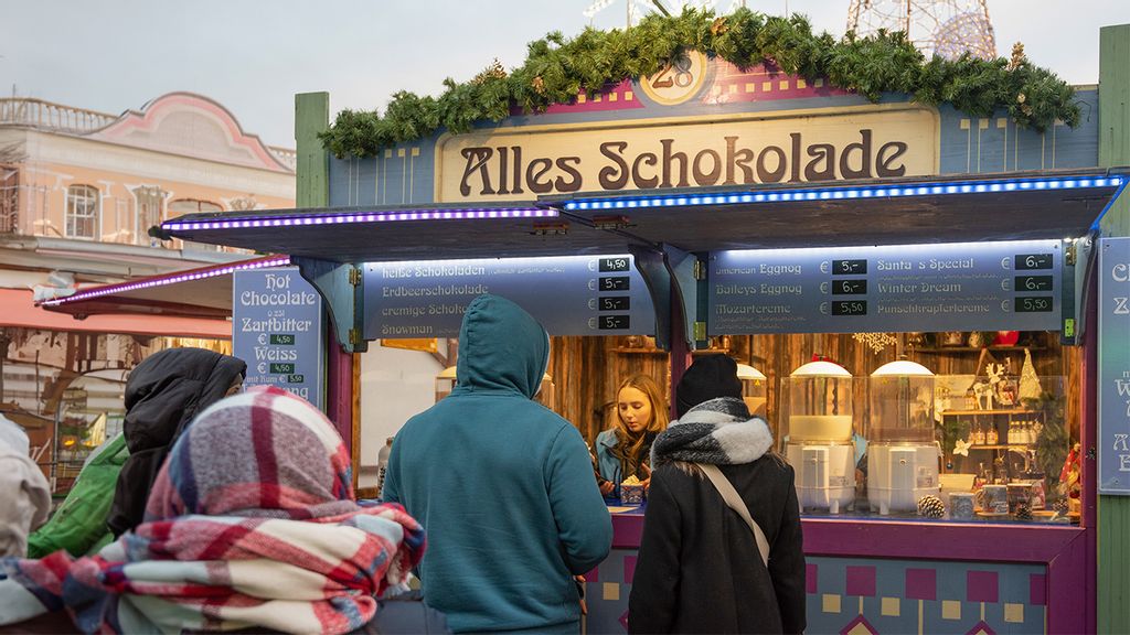 Eine Mitarbeiterin in der Hütte am Wintermarkt umgeben von mehreren Kund*innen vor der Hütte