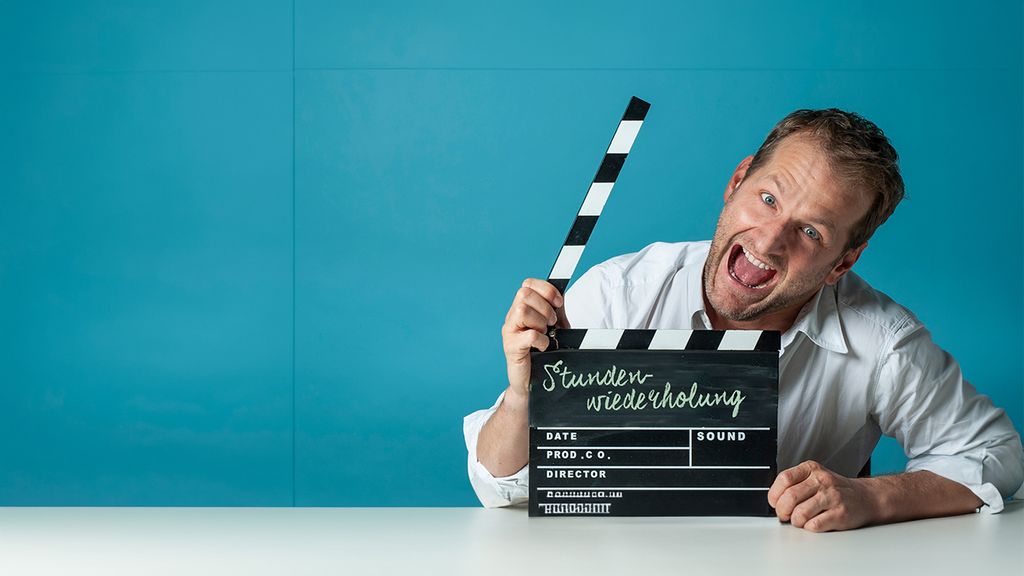 Andreas Ferner hält eine Filmklappe in der Hand und lacht in die Kamera.