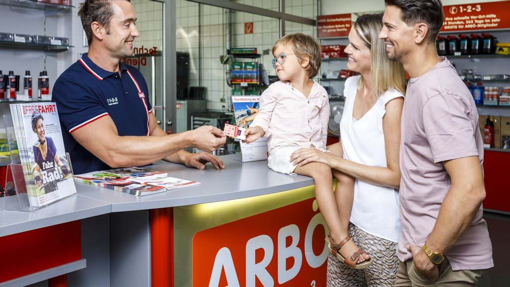 Familie beim Einlösen des Vorteils - Kind überreicht die Mitgliedskarte an den Shopmitarbeiter