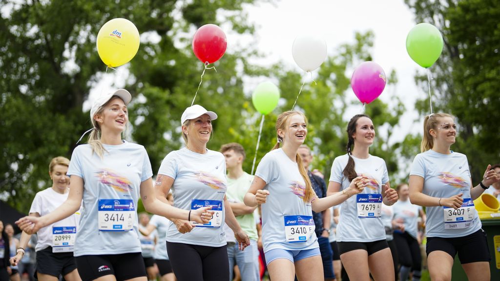 Fünf Frauen in Sportkleidung mit Startnummern auf deren T-Shirts und Luftballonen im Hintergrund