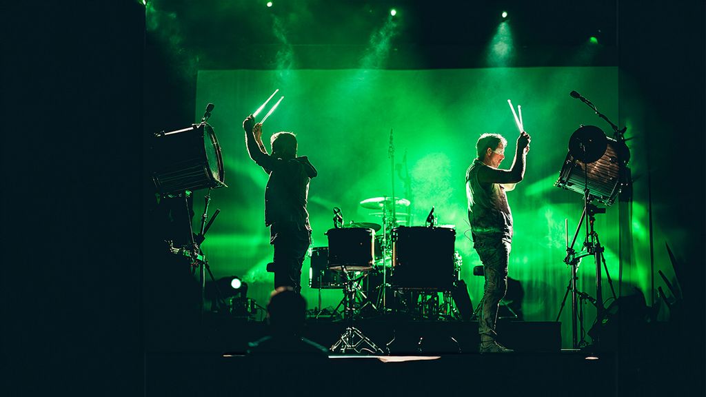 Zwei Schlagzeugspieler auf einer Bühne in grünem Licht