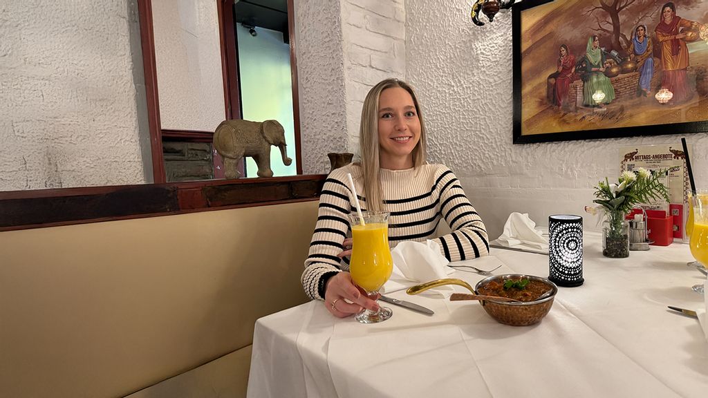 © stadt wien marketing gmbh Frau sitzt an einem gedeckten Tisch mit indischen Speisen