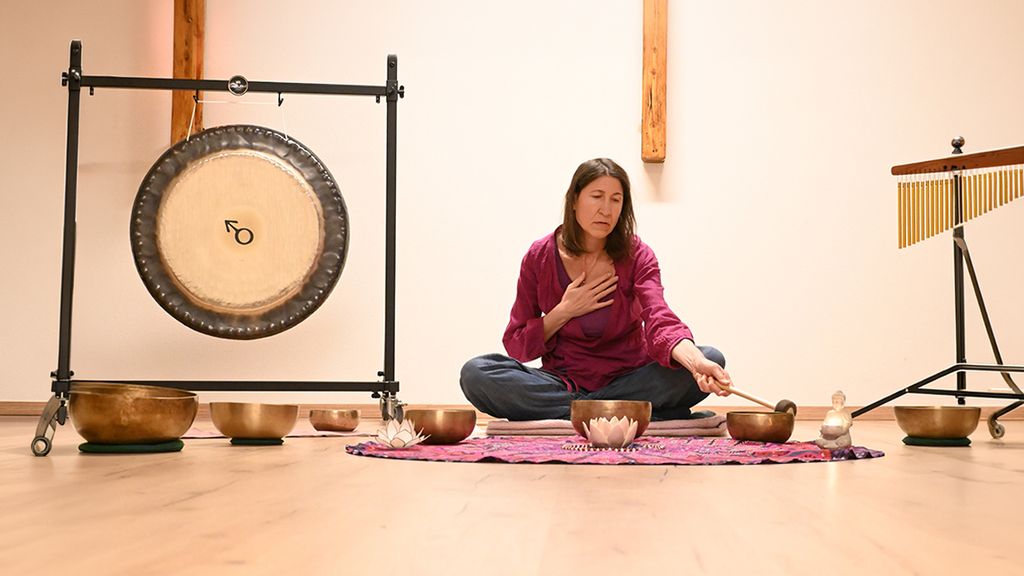 Eine Frau sitzt auf einer Yoga-Matte bei einer Klangschalen-Therapie
