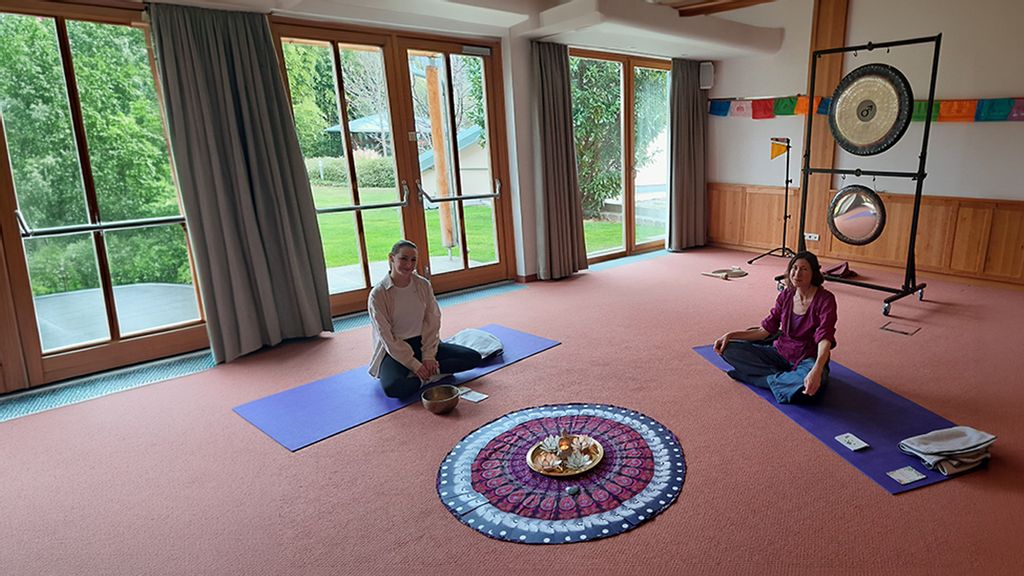 Zwei Frauen sitzen jeweils auf einer Yoga-Matte bei einer Klangschalen-Therapie