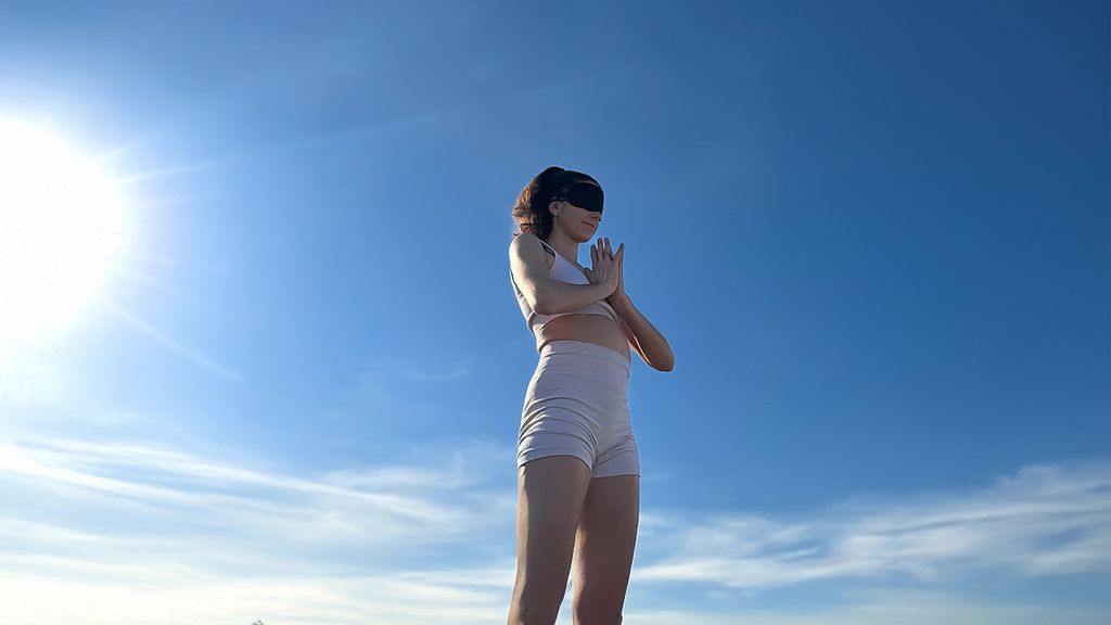 Eine Frau bei Sonnenschein in Yoga-Position mit Augenbinde