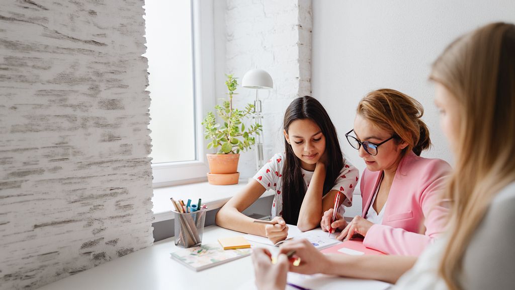 Zwei Mädchen sitzen mit der Nachhilfe-Lehrerin an einem Tisch zusammen und lernen