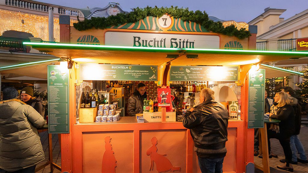 Weihnachtsmarkt-Hütte mit einem Verkäufer, umgeben von Personen, die links, rechts und davor stehen.