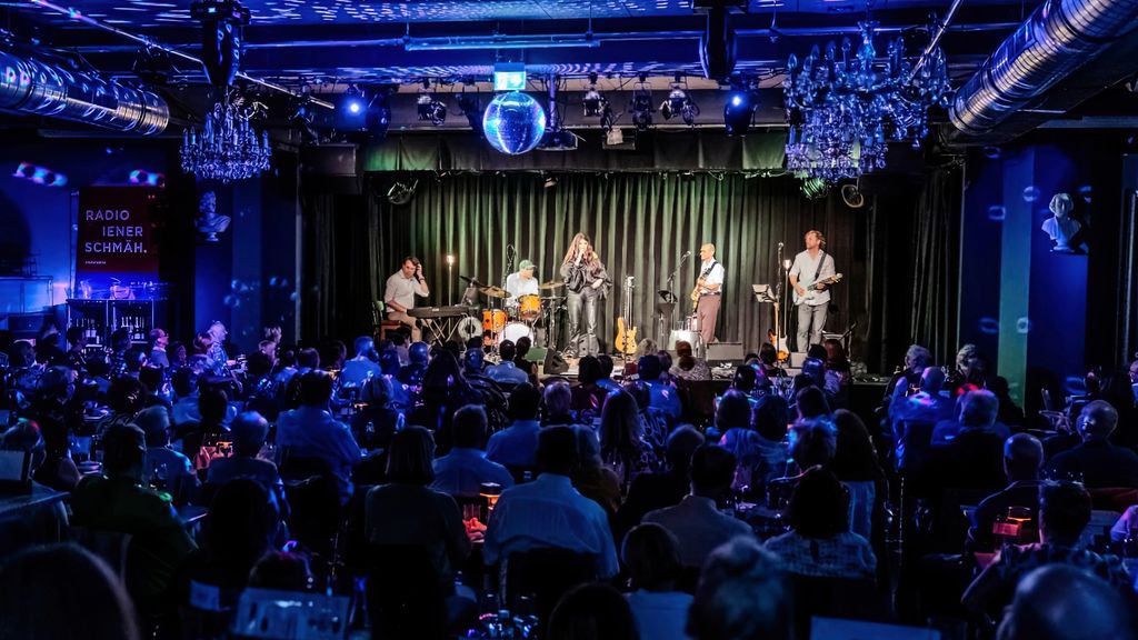 Eine Band spielt auf er Bühne vor Publikum an den Tischen