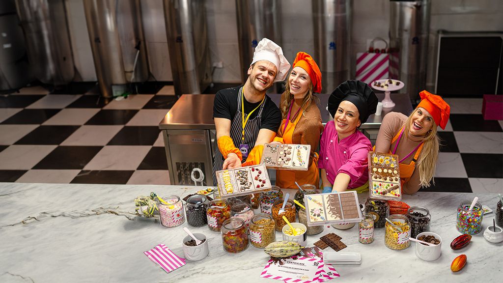 mehrere Frauen in rosa Schürzen halten Pralinen in der Hand und stehen vor einem Tisch