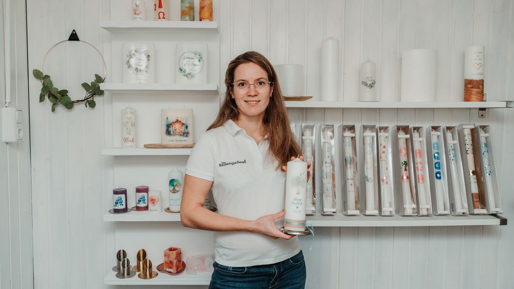 Verkäuferin der Kerzengießerei hält eine verzierte Kerze in der Hand und lächelt.