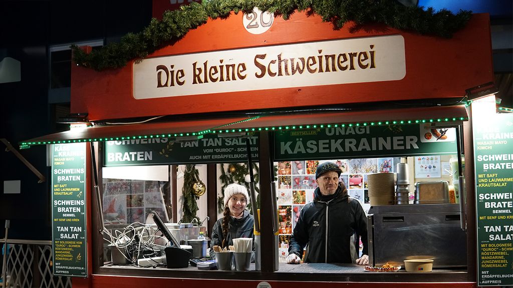 PlatzhalterWeihnachtsmarkt-Stand bei Nacht mit Verkäufer*innen hinter dem Tresen.
