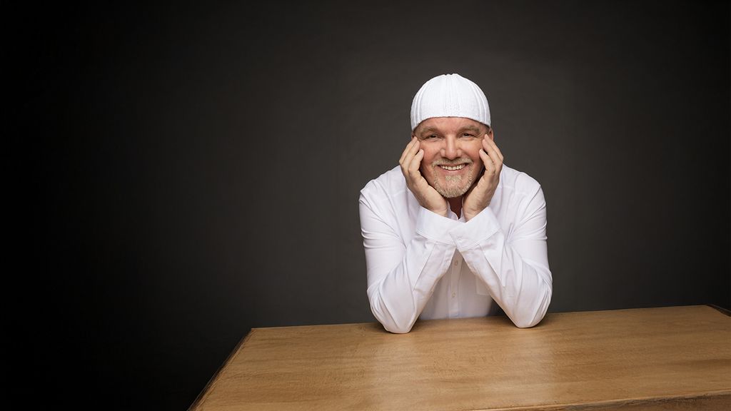 DJ Ötzi lächelt, stützt das Gesicht mit den Händen und sitzt an einem Tisch