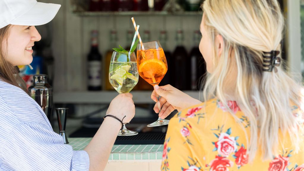 zwei Frauen stoßen mit Cocktailgläsern vor einer Bar an