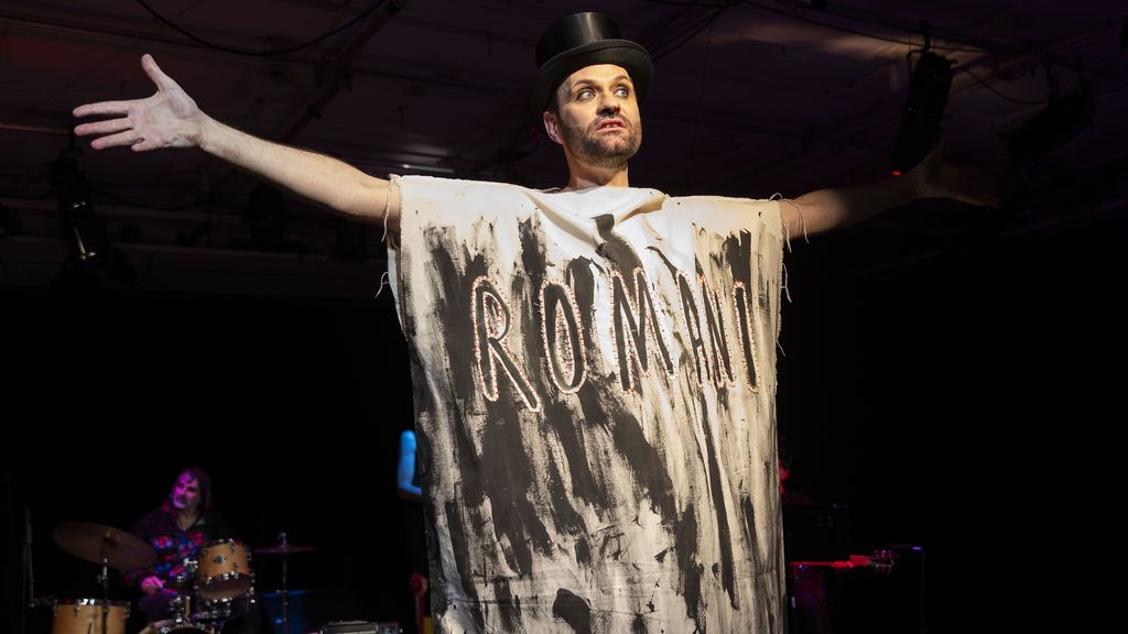 Ein Mann mit schwarzem Hut und weiß-schwarzem Umhang mit der Aufschrift Roma auf der Bühne