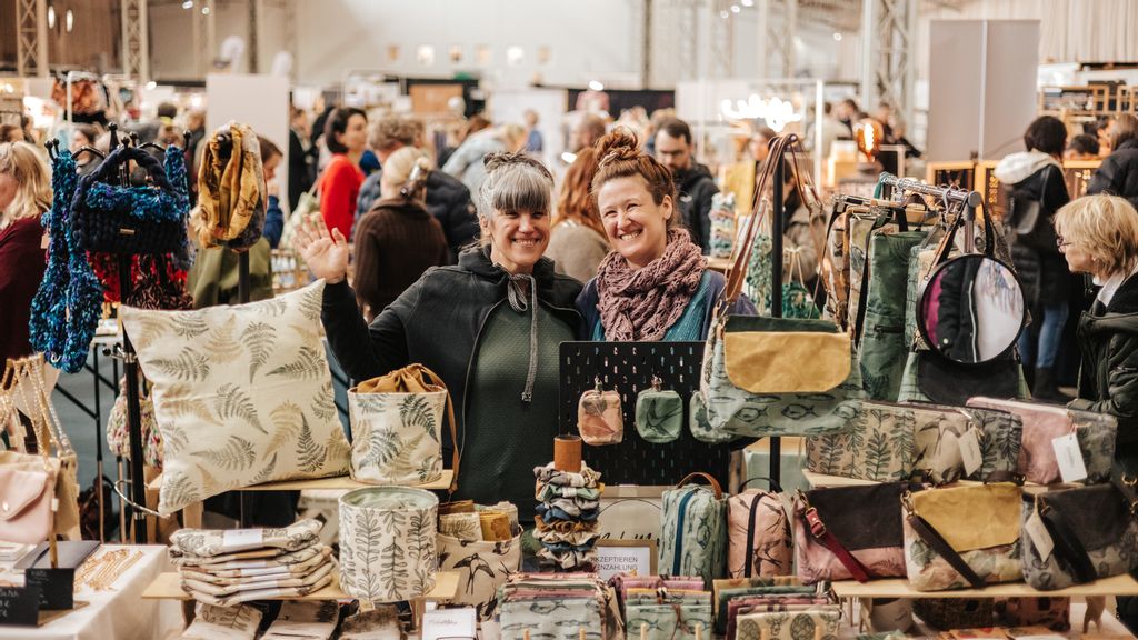 Zwei Aussteller*innen lächelnd bei ihrem Verkaufsstand am Designmarkt.