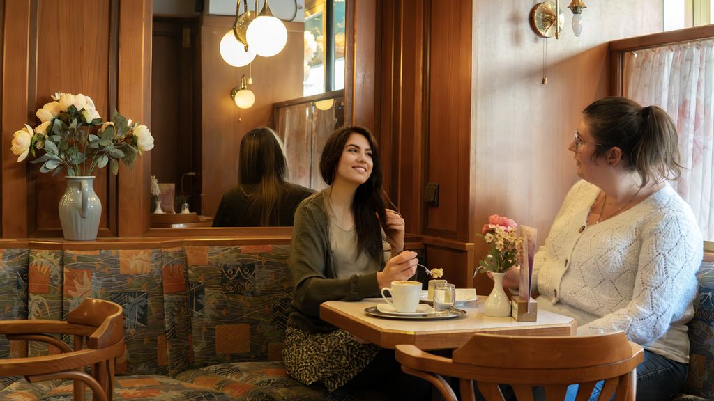 Zwei Frauen sitzen bei Café und Kuchen an einem Tisch