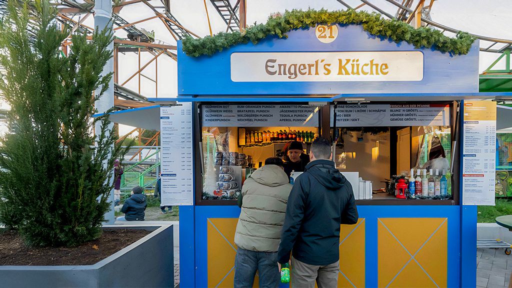 Weihnachtsmarkt-Hütte mit einem Verkäufer, umgeben von Personen.