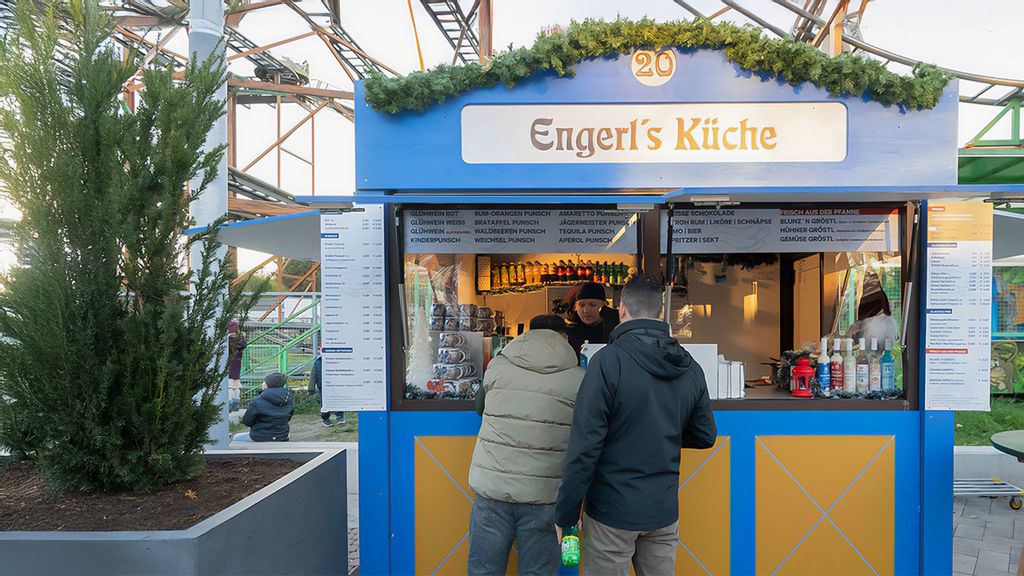 Weihnachtsmarkt-Hütte mit einem Verkäufer, umgeben von Personen.