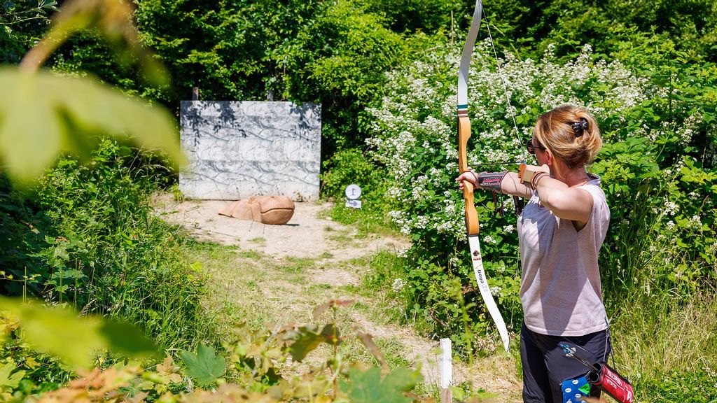 Frau zielt mit Pfeil und Bogen auf eine Zielscheibe im Wald