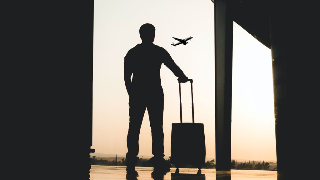 Ein Mann steht mit einem Koffer am Flughafen
