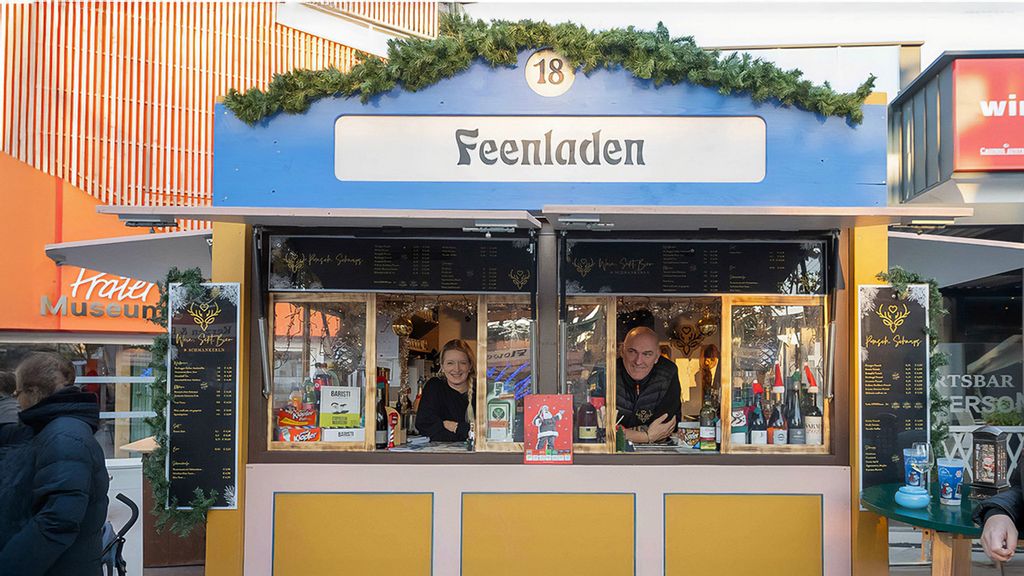 Weihnachtsmarkt-Hütte mit Verkäufer*innen, umgeben von Personen.