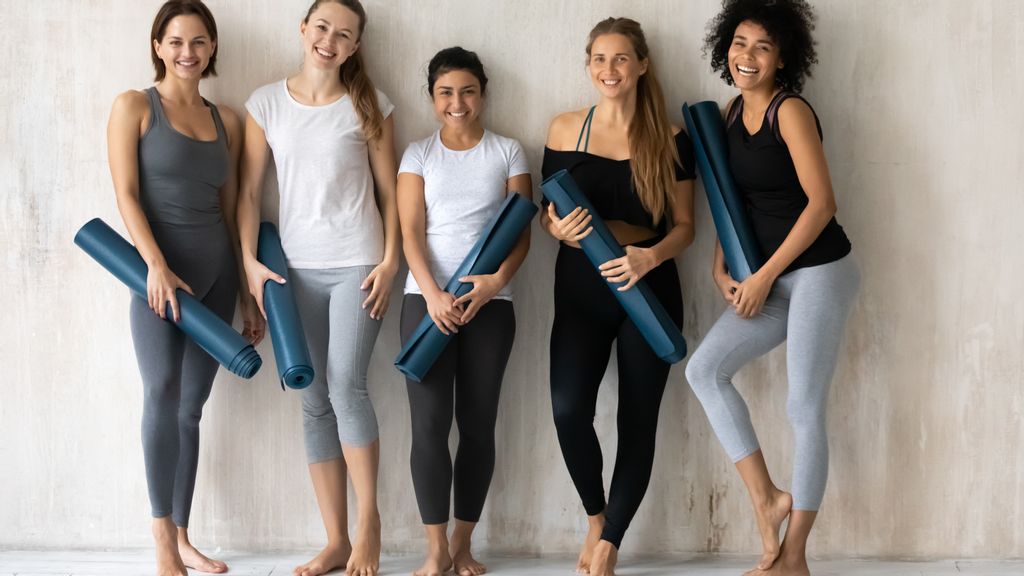 Mehrere Frauen lehnen mit einer Yogamatte gegen eine beige Wand