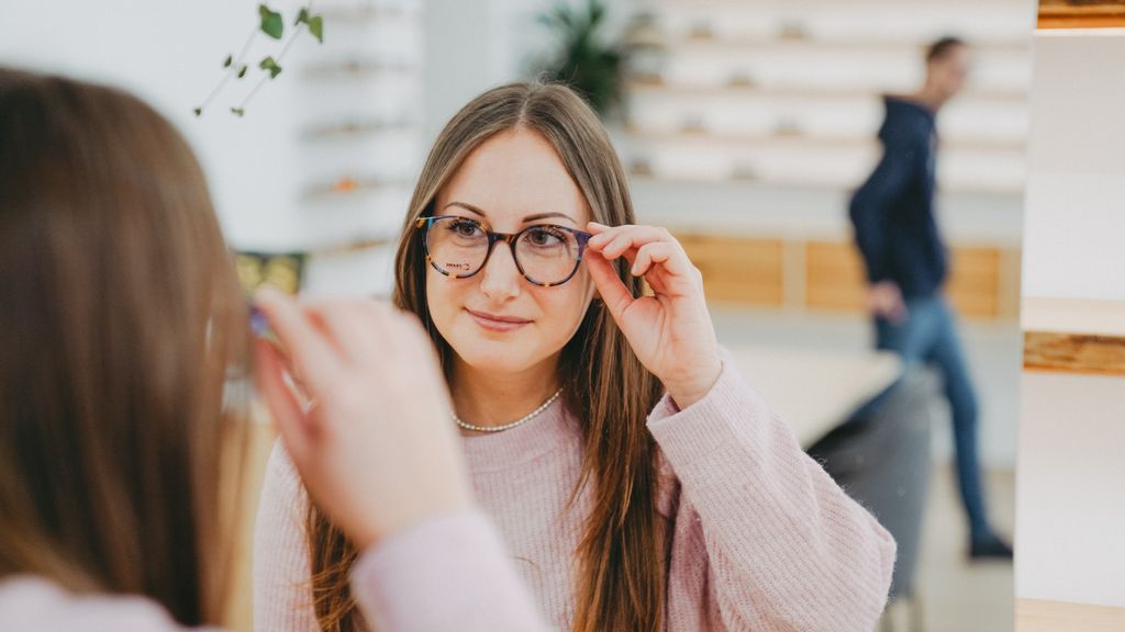 Frau schaut sich mit ihrer Brille beim Optiker in den Spiegel