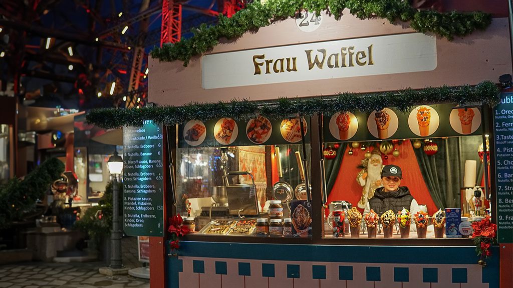 Weihnachtsmarkt-Stand bei Nacht mit Verkäuferin hinter dem Tresen.