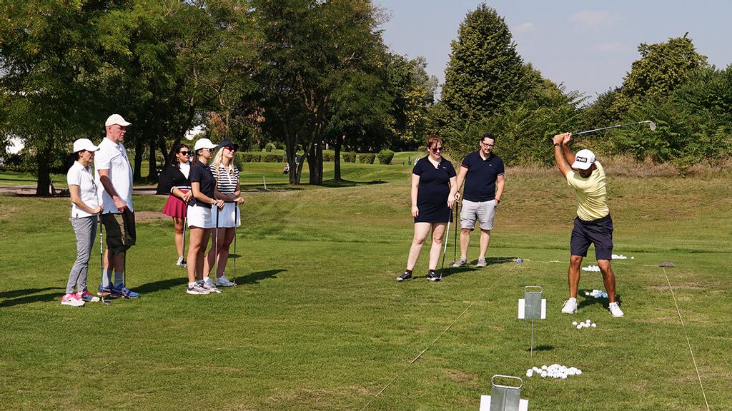 Eine Gruppe an Personen mit einem Golftrainer auf einem Golfplatz