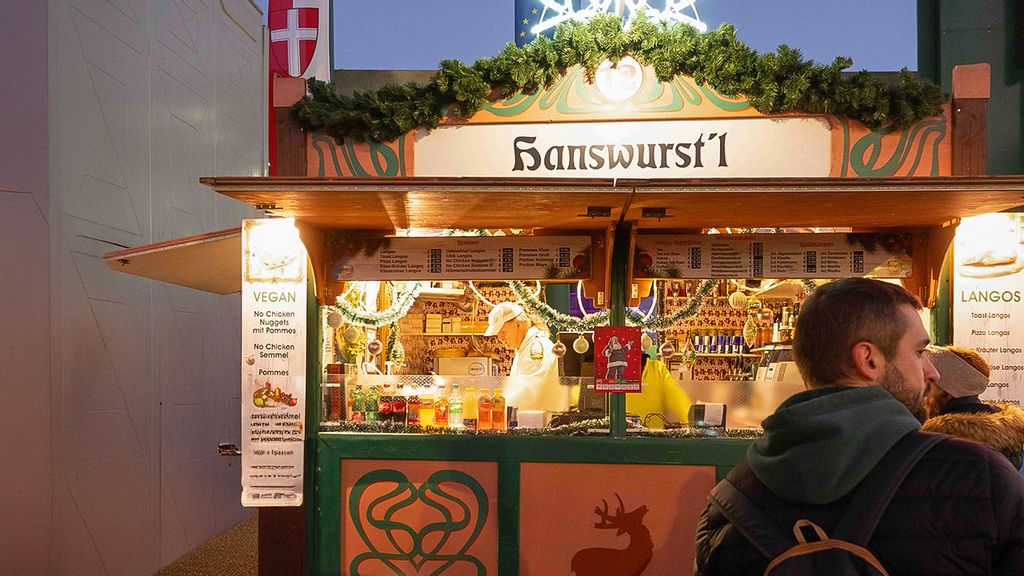 Zwei Mitarbeiter*innen in der Hütte und mehrere Personen vor bzw. neben der Hütte am Wintermarkt