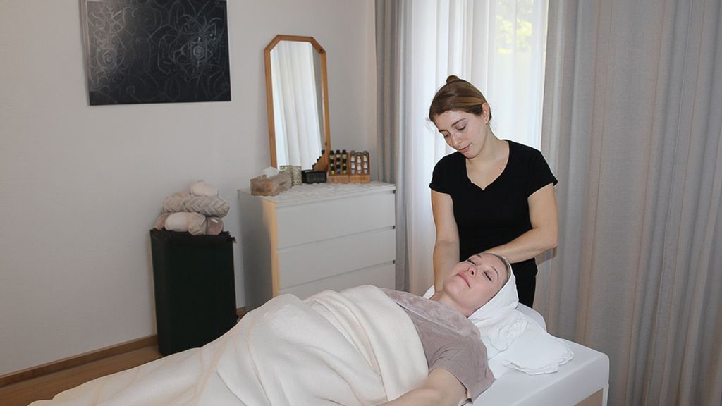 Frau liegt am Rücken und lässt sich den Nacken von der Masseurin massieren