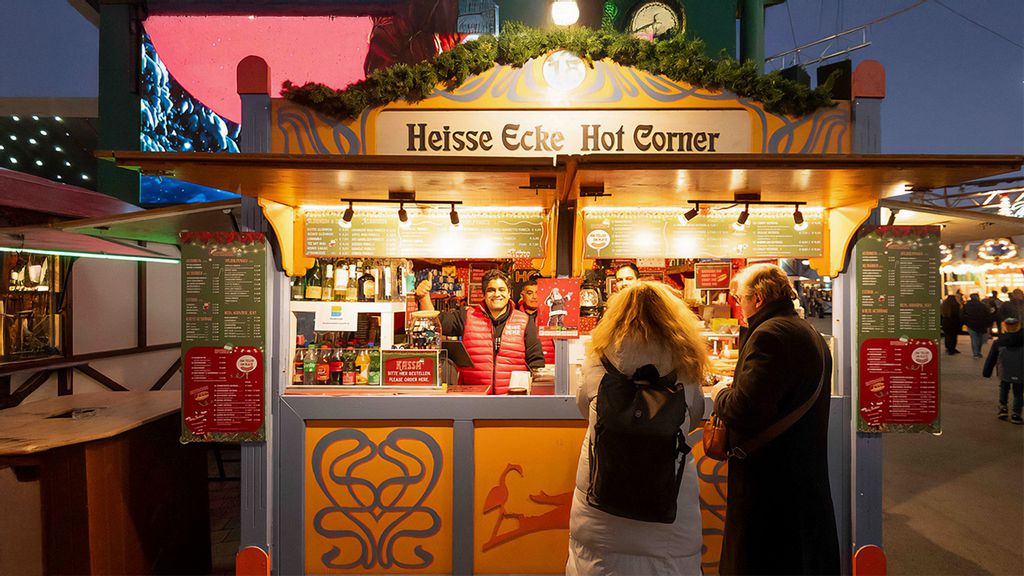 Weihachtsmarkt-Hütte mit Verkäufern, umgeben von Personen. 