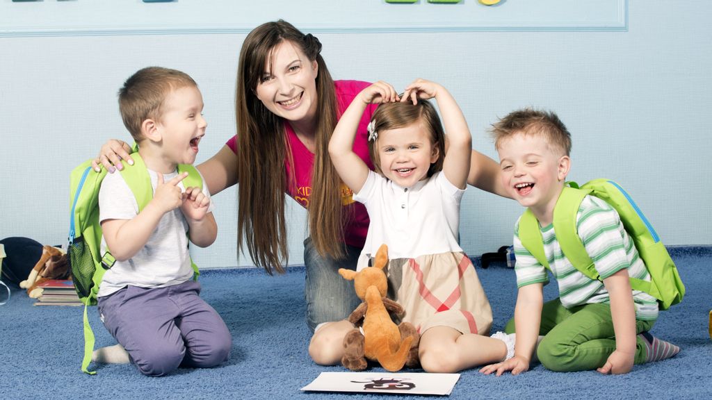 Drei Kinder mit einer Lehrerin sitzend am Boden