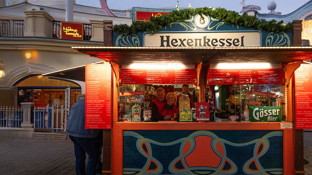 Weihnachtsmarkt-Hütte mit zwei Verkäufern und einer Verkäuferin, umgeben von Personen.