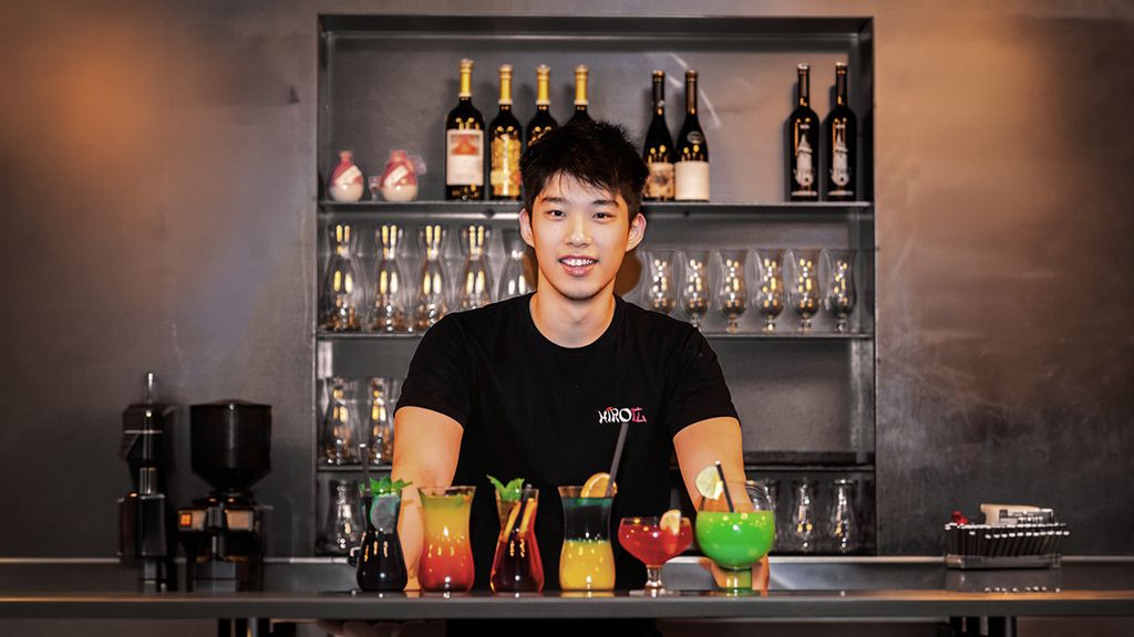 Barkeeper steht hinter einer Bar und präsentiert mehrere bunte Cocktails 