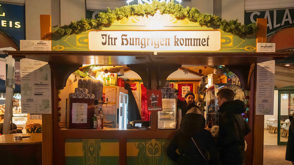 Ein Mitarbeiter in der Hütte und zwei Personen vor der Hütte am Wintermarkt