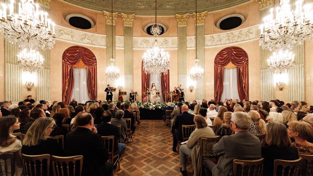Sängerin und Orchester in barocken Kostümen auf Bühne im prunkvollen Saal