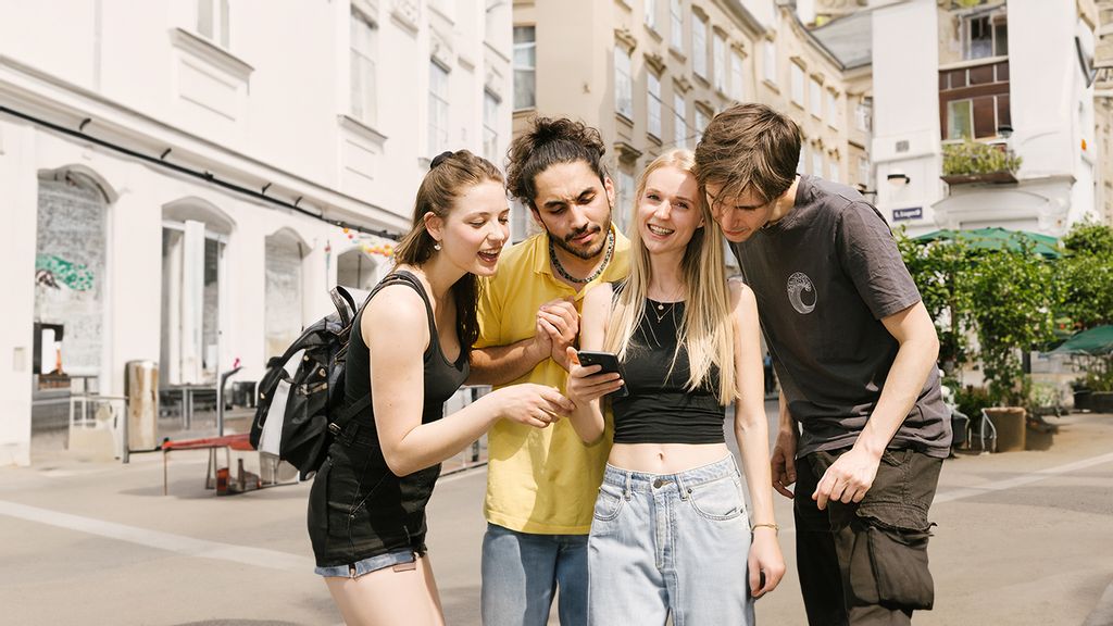 Gruppe von zwei Frauen und zwei Männern die mit einem Smartphone in der Hand Rätsel lösen
