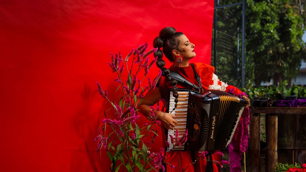 Seitlich stehende Frau in rotem Kleid hält spielt auf einem Akkordeon.