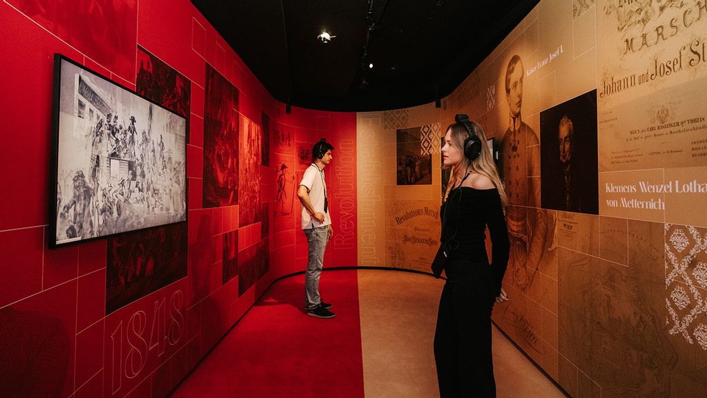 Ein Frau und ein Mann mit Kopfhörer erkunden die Johann Strauss Ausstellung