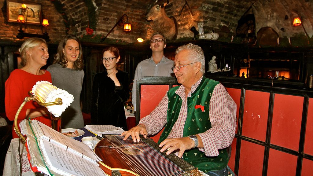 Mann spielt auf einer Zitter im Piaristenkeller. Drei Frauen und ein Mann stehen daneben 