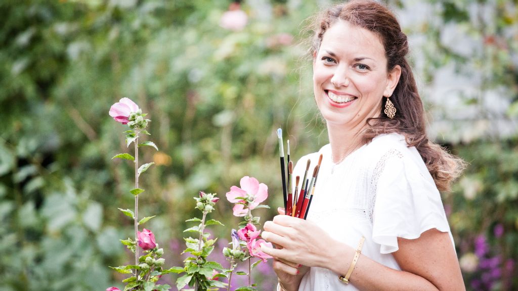 Mentorin Katalin Kardos hält Pinsel in der Hand und lächelt in die Kamera