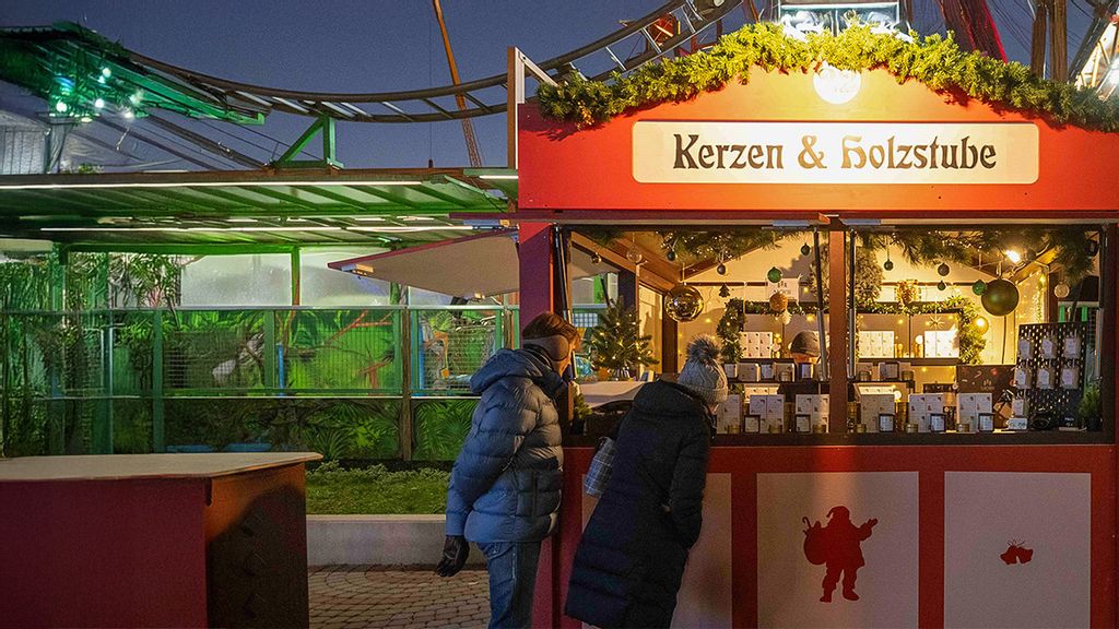 Weihnachtsmarkt-Hütte mit einem Verkäufer und zwei Kund*innen, die sich Produkte ansehen.