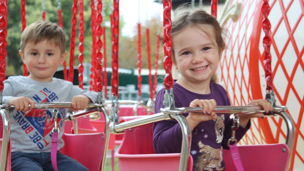 Ein lächelndes Mädchen und ein Junge hintereinander im Kettenkarussell