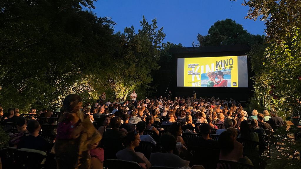 Im Park sitzendes Publikum vor einer beleuchteten Leinwand