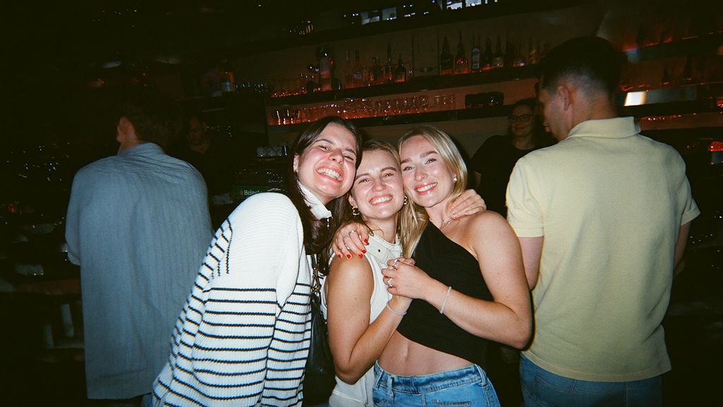 Drei junge Frauen umarmend und lächelnd in einer Bar