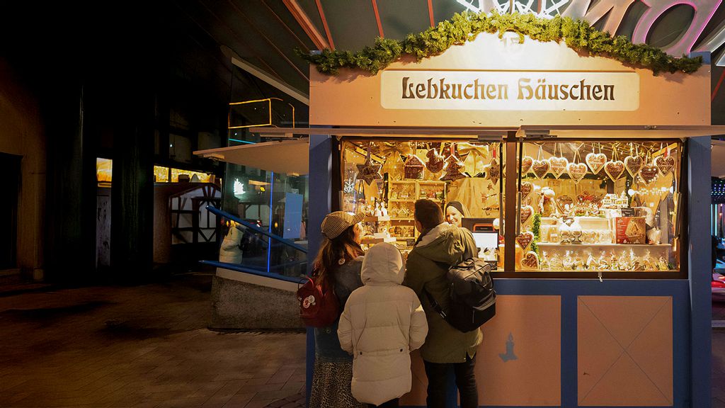 Weihnachtsmarkt-Hütte mit Verkäuferin, umgeben von Personen.