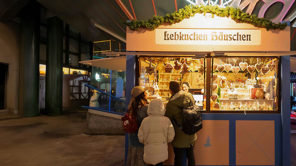 Weihnachtsmarkt-Hütte mit Verkäuferin, umgeben von Personen.