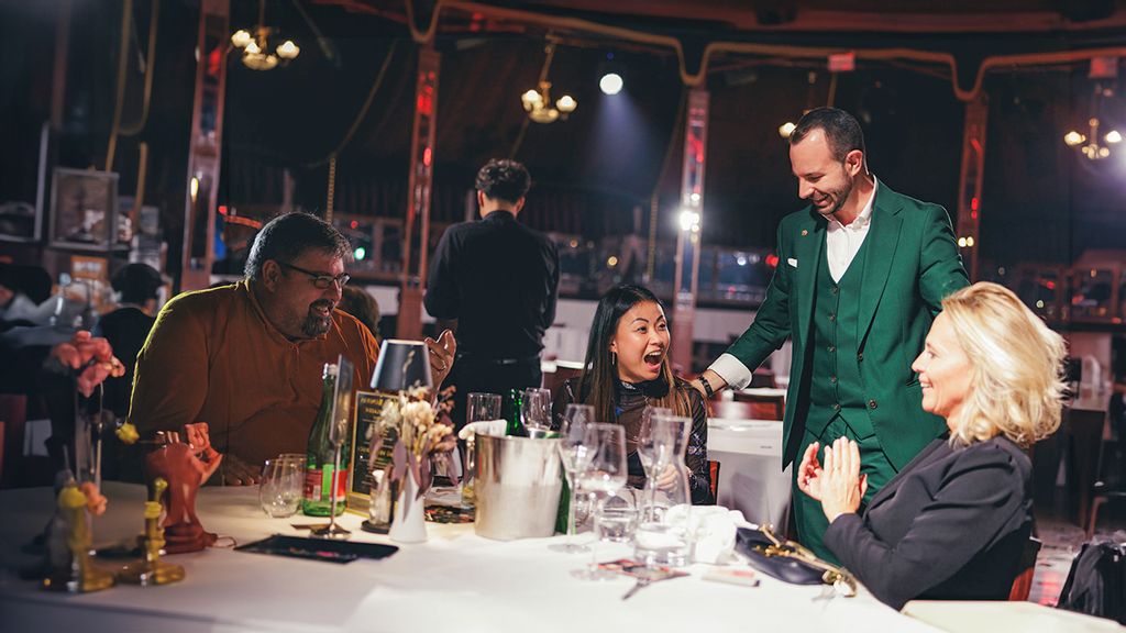 Ein Magier steht nach einem Trick bei einem Besucher*innen-Tisch